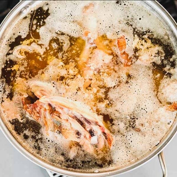 a pot of stock on the stove with foam and fat collecting on the top.