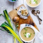 two bowls of soup with leeks and scallions and a bulb of roasted garlic