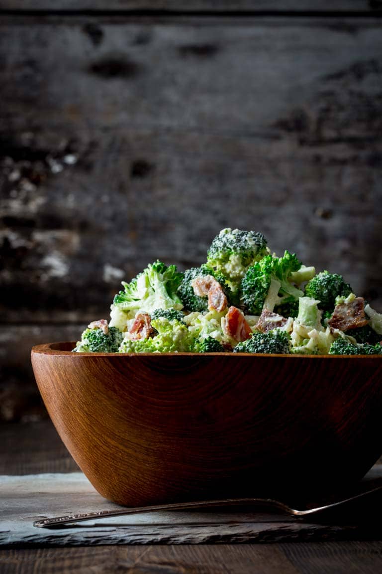 a side view of a wooden bowl heaped with broccoli salad with bacon