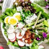 close up of composed salad with eggs, asparagus, radishes and yogurt dill dressing on top