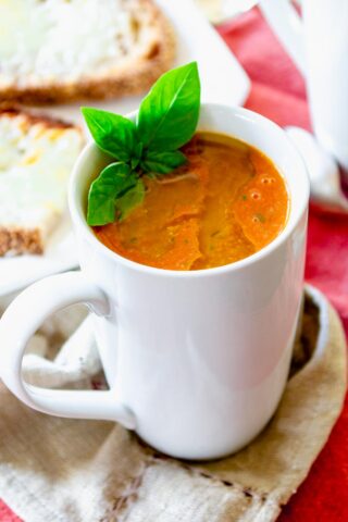 a white mug with tomato soup with basil garnish