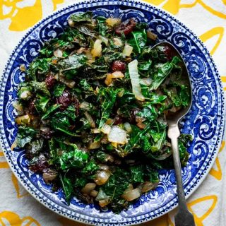 A blue china dish with sauteed kale in it, on a yellow and white dish towel
