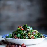Side view of a bowl of kale with cranberries and balsamic vinegar on a gray table with a gray background