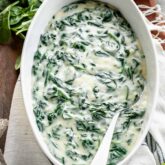 creamed spinach in oval white serving dish with silver serving spoon