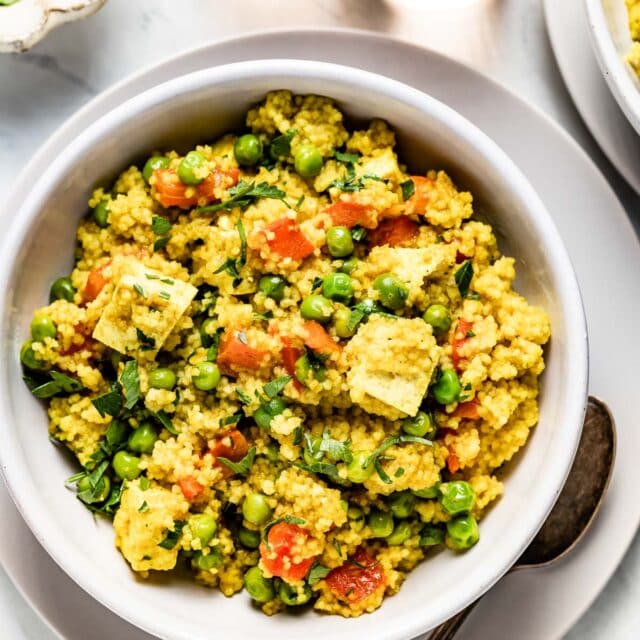 a white bowl with curried couscous with tofu with wine on a white table