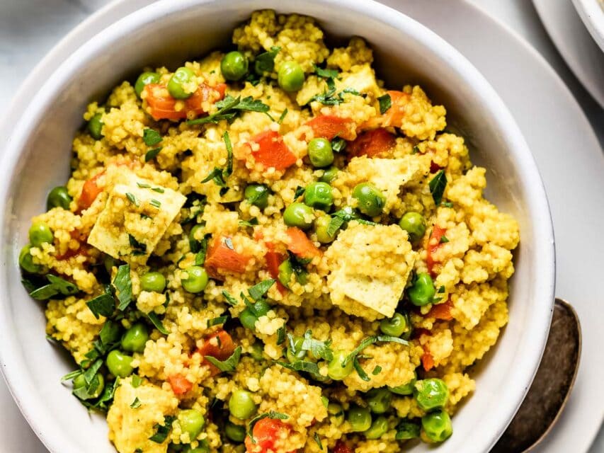 a white bowl with curried couscous with tofu with wine on a white table