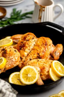 cast iron skillet with the spatchcocked chicken in it with lemon wedges
