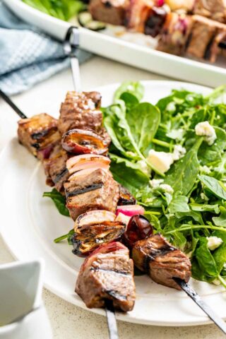 a plate with spinach and blue cheese salad with two steak kebabs