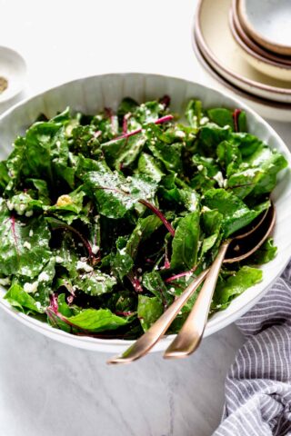 beet greens in a white bowl with tongs