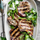 a platter of pork chops with arugula salad from overhead on a table with a large serving fork