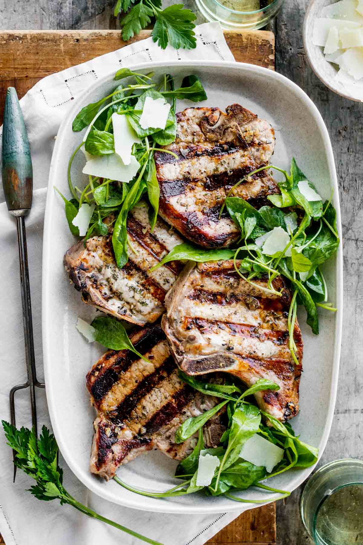 a platter of pork chops with arugula salad from overhead on a table with a large serving fork