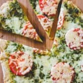 A slice of pizza sitting on top of a wooden cutting board, with Pesto