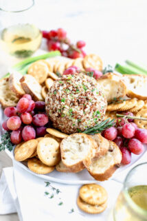 side view of cheeseball on a platter with crackers and grapes