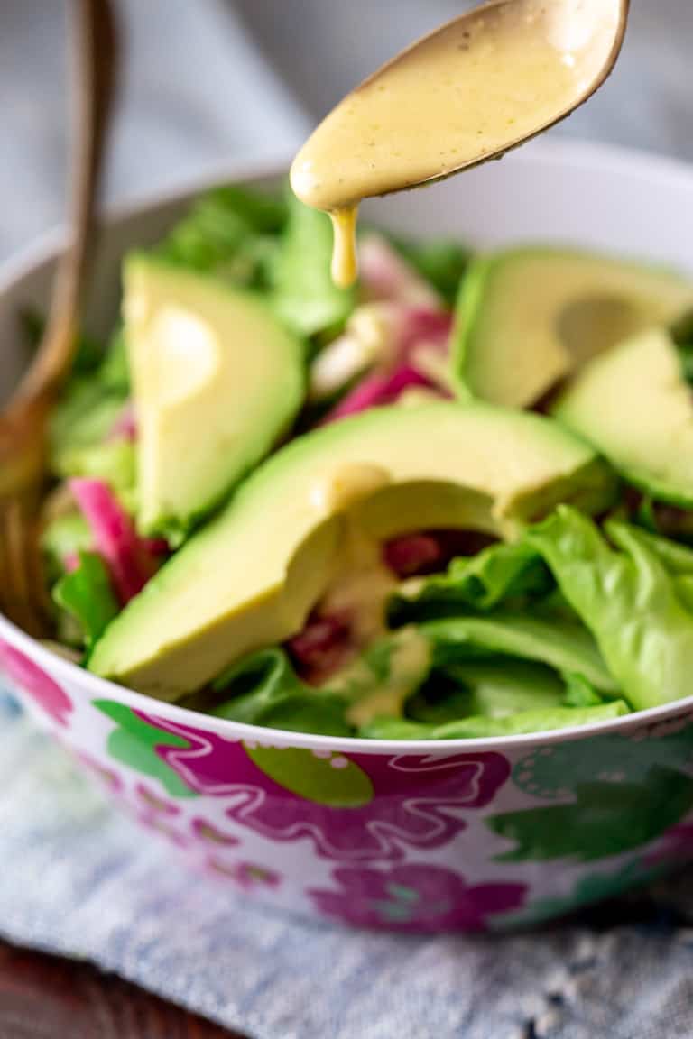 A salad with avocado on it with dressing being spooned on top