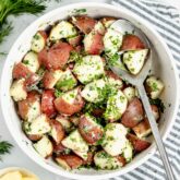 Steamed potatoes with fresh herbs in circular white bowl.
