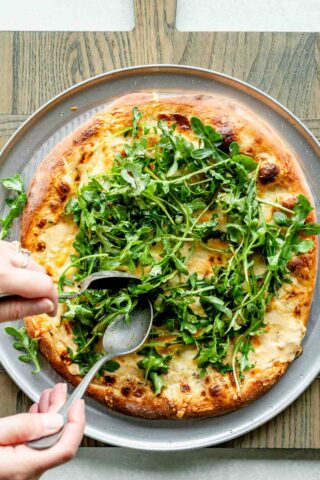 topping the pizza with arugula salad