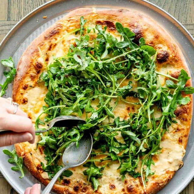 topping the pizza with arugula salad