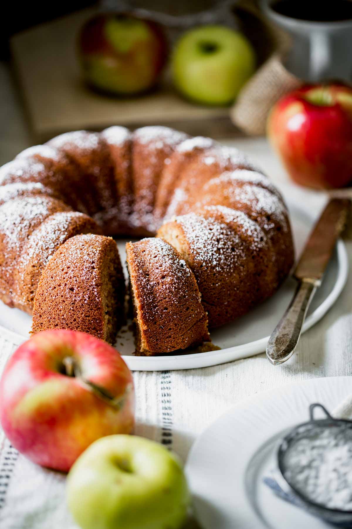 applesauce snack cake on a white platter with a knife and apples on the table