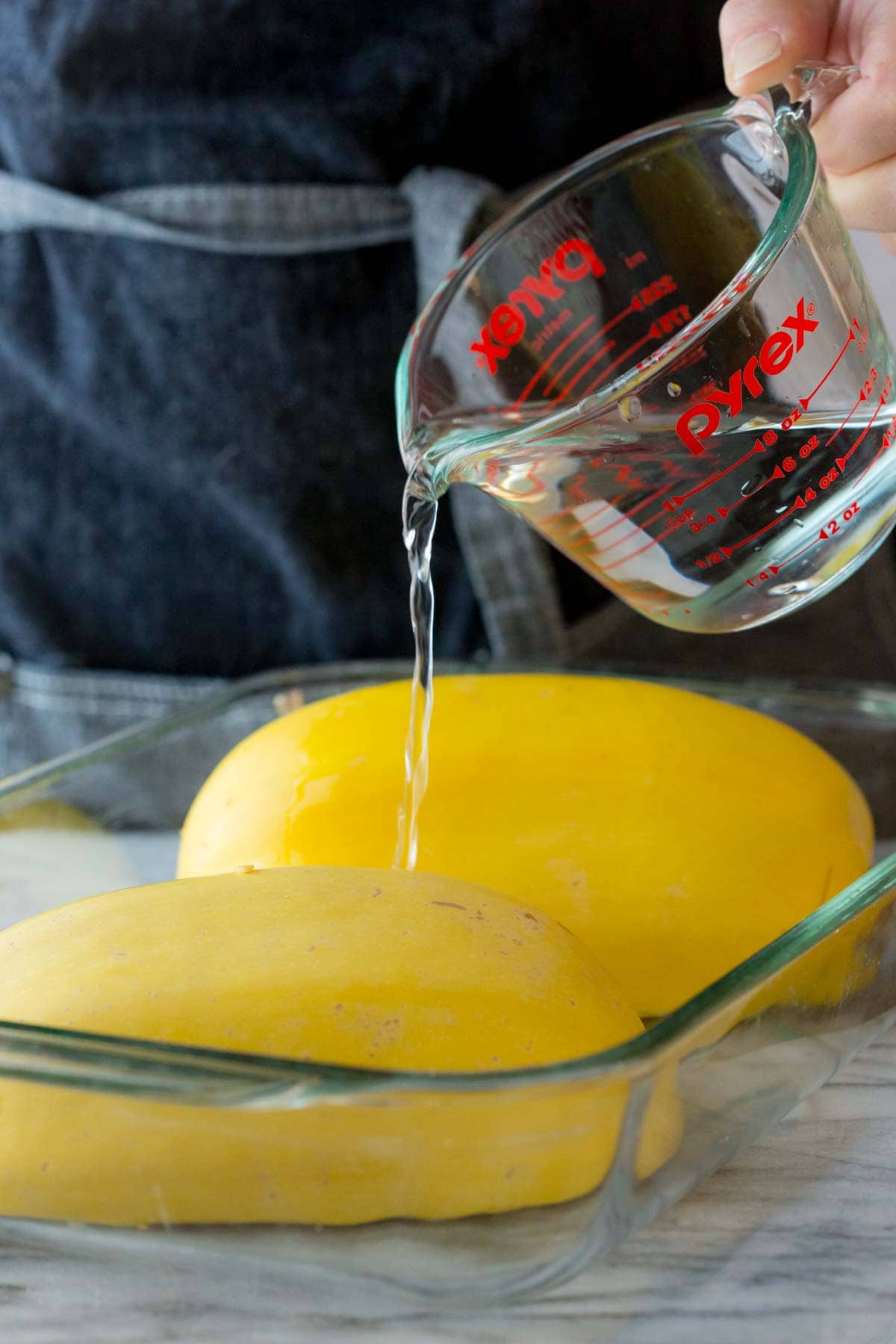 pouring water into the baking dish with the spaghetti squash in it
