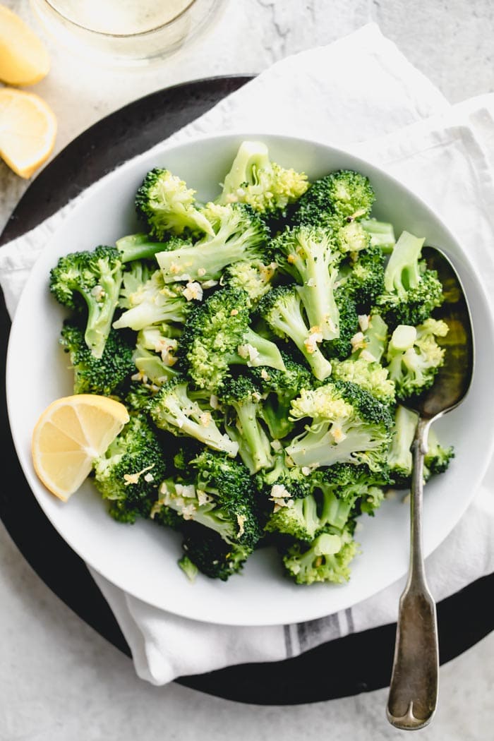 overhead closeup of broccoli in a white bowl with a lemon wedge