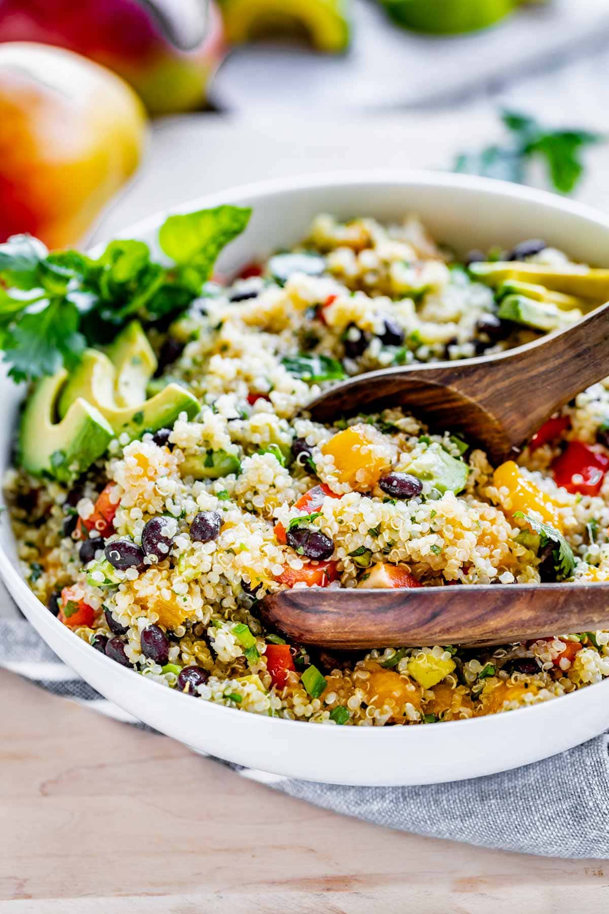 side view of the quinoa salad in a white view with wooden salad tongs