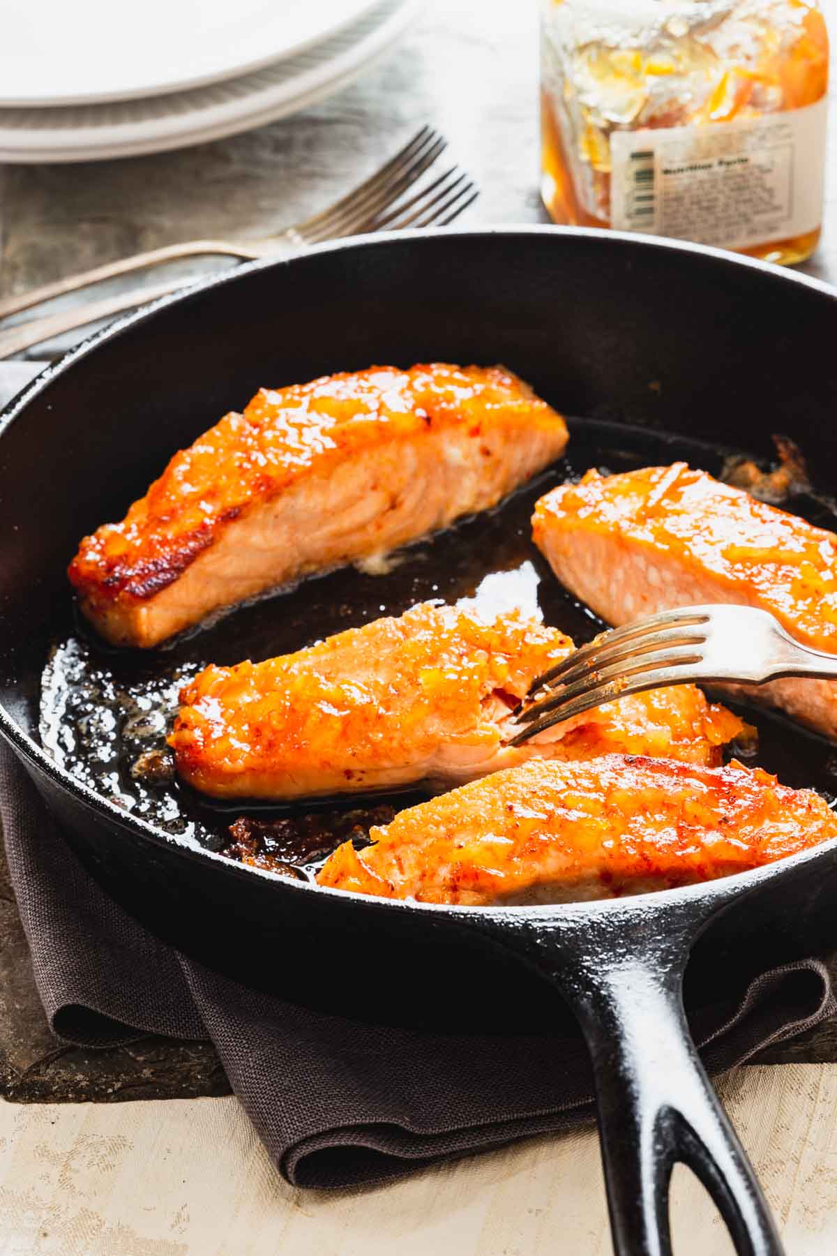a cast iron skillet with four pieces of salmon, a fork is flaking one of the pieces