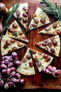 the pizza cut into slices with a bunch of grapes and sprigs of rosemary