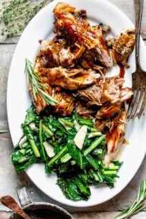 chunks of slow roasted pork with sauteed mustard greens and gravy drizzled on it on a white oval platter