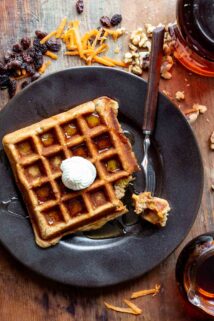 overhead view of a waffle on a black plate from overhead with cream cheese piped on top and drizzled with maple syrup