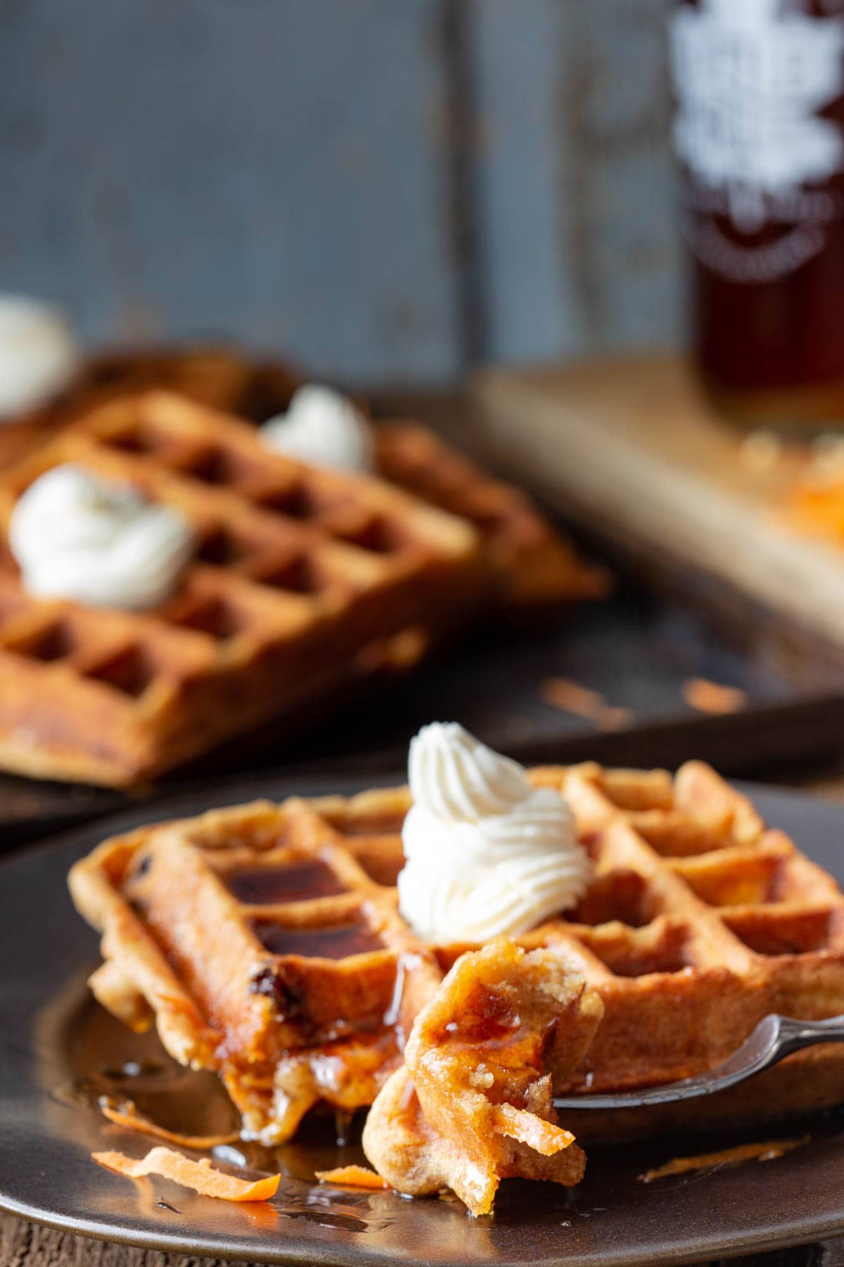 a bite of the carrot cake waffle on a fork, drizzled with syrup resting on the plate with the waffle