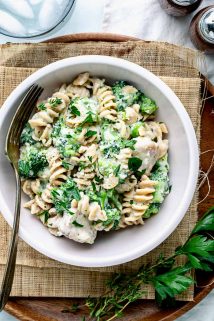 A close up of a pale pink bowl with spiral pasta and chicken alfredo with broccoli