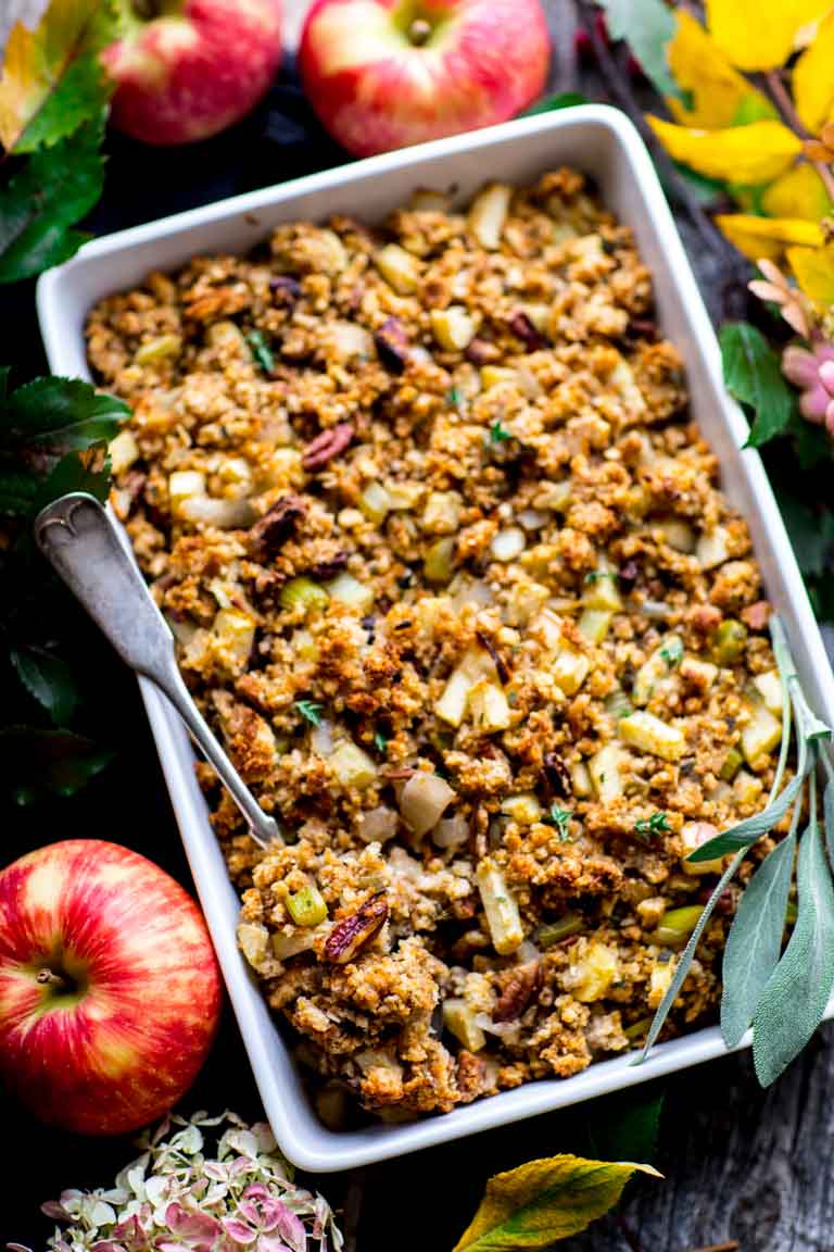 a white casserole dish filled with stuffing with apples around it