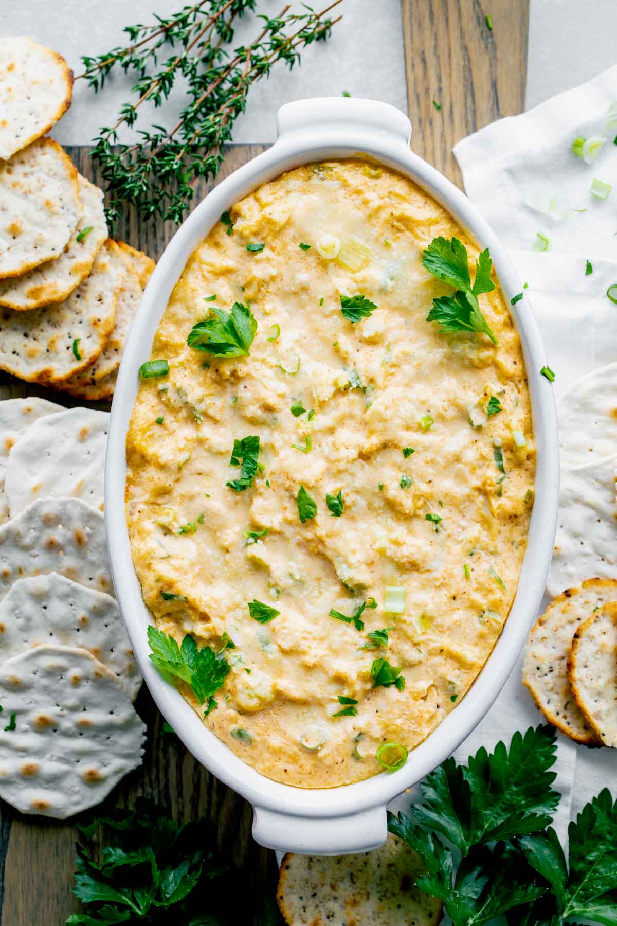 the baked crab dip on a cutting board with crackers around it