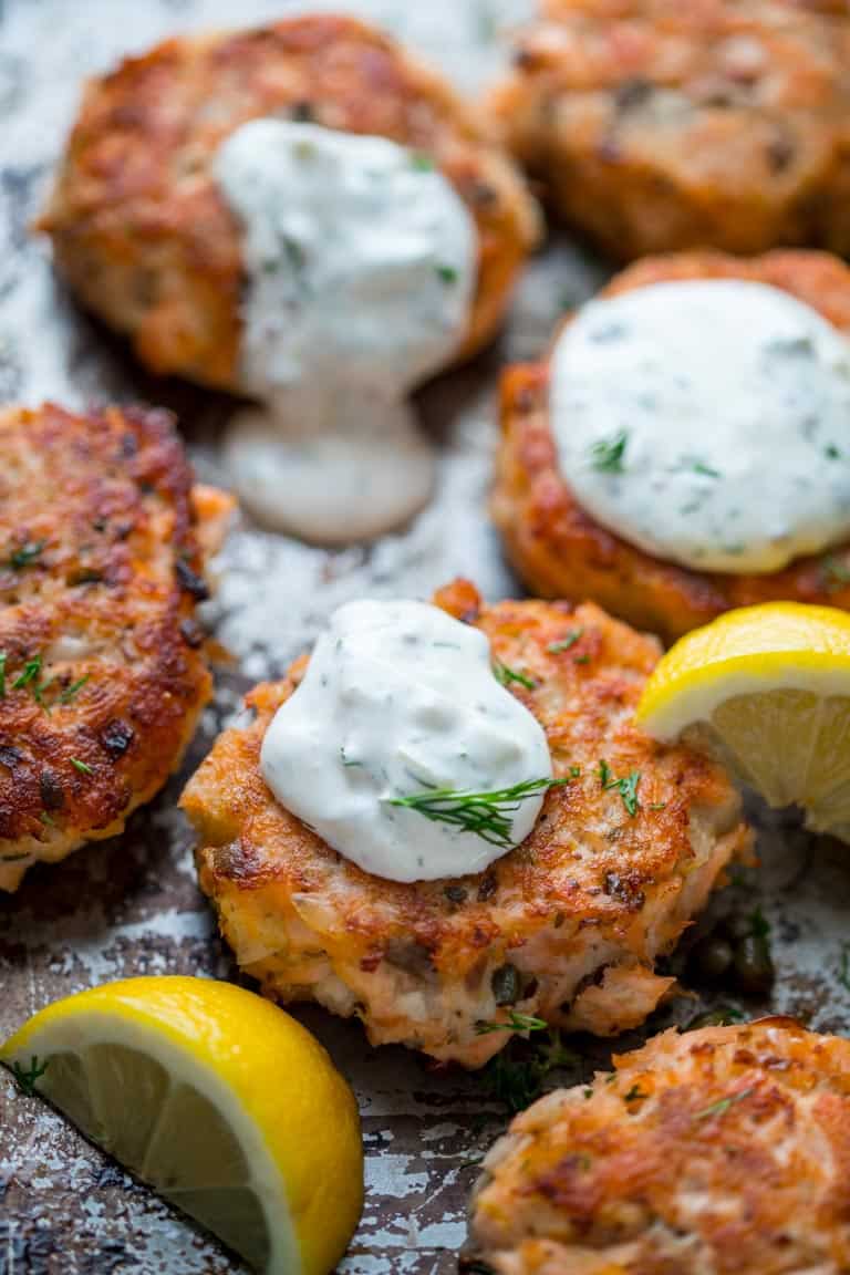 A close up of salmon cakes on a sheet pan from a three quarter overhead view beside lemon slices