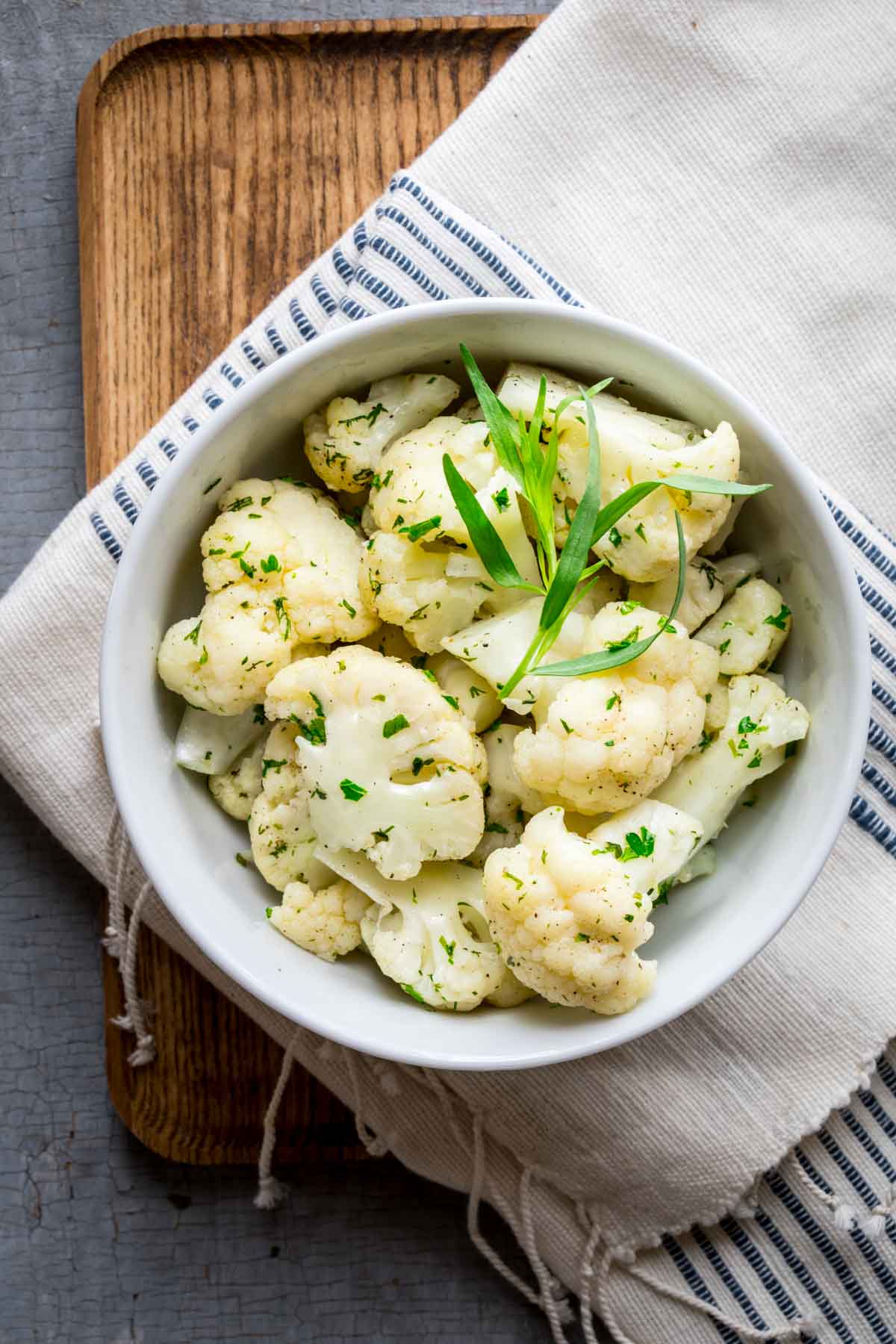 white bowl of steamed cauliflower with tarragon sprig on top