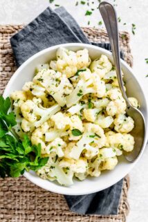 white bowl with herbed cauliflower with sprigs of parsley and a spoon resting in the bowl