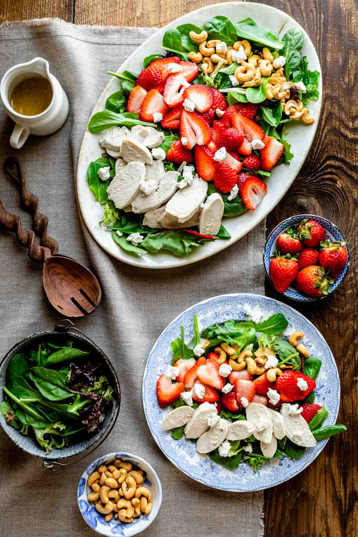a platter with the salad comosed on it with a separate plate with a serving on it overhead on a table with salad tongs