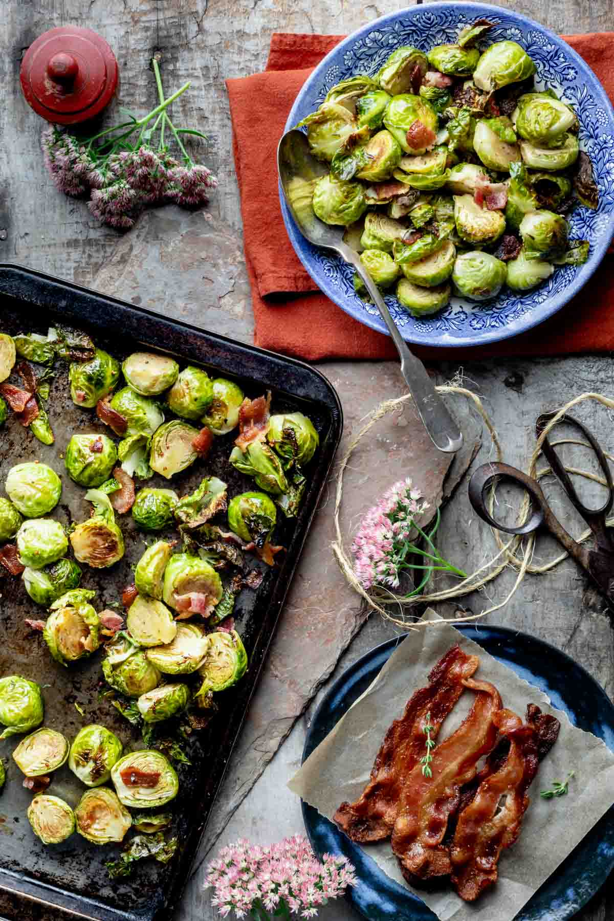 overhead of the table with sheet pan of the Brussels on it, blue bowl with more brussels and a tray of cooked bacon