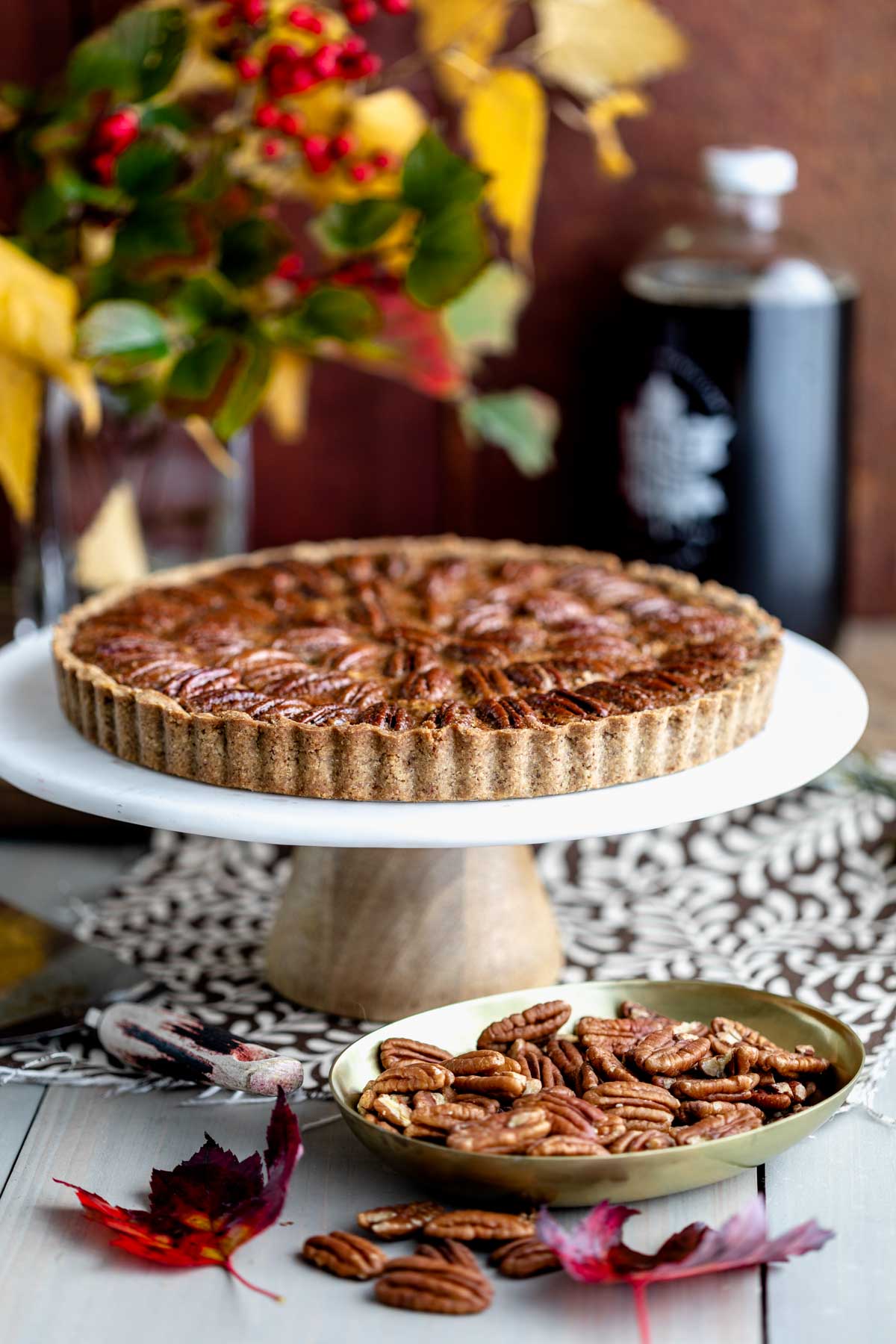 side view of the tart on a tart stand with fall floral arrangement in background