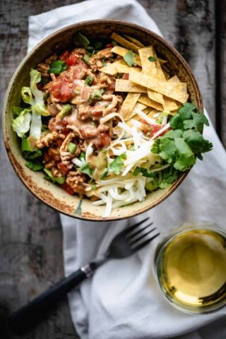 An overhead view of a serving of healthy taco salad with a glass of white wine