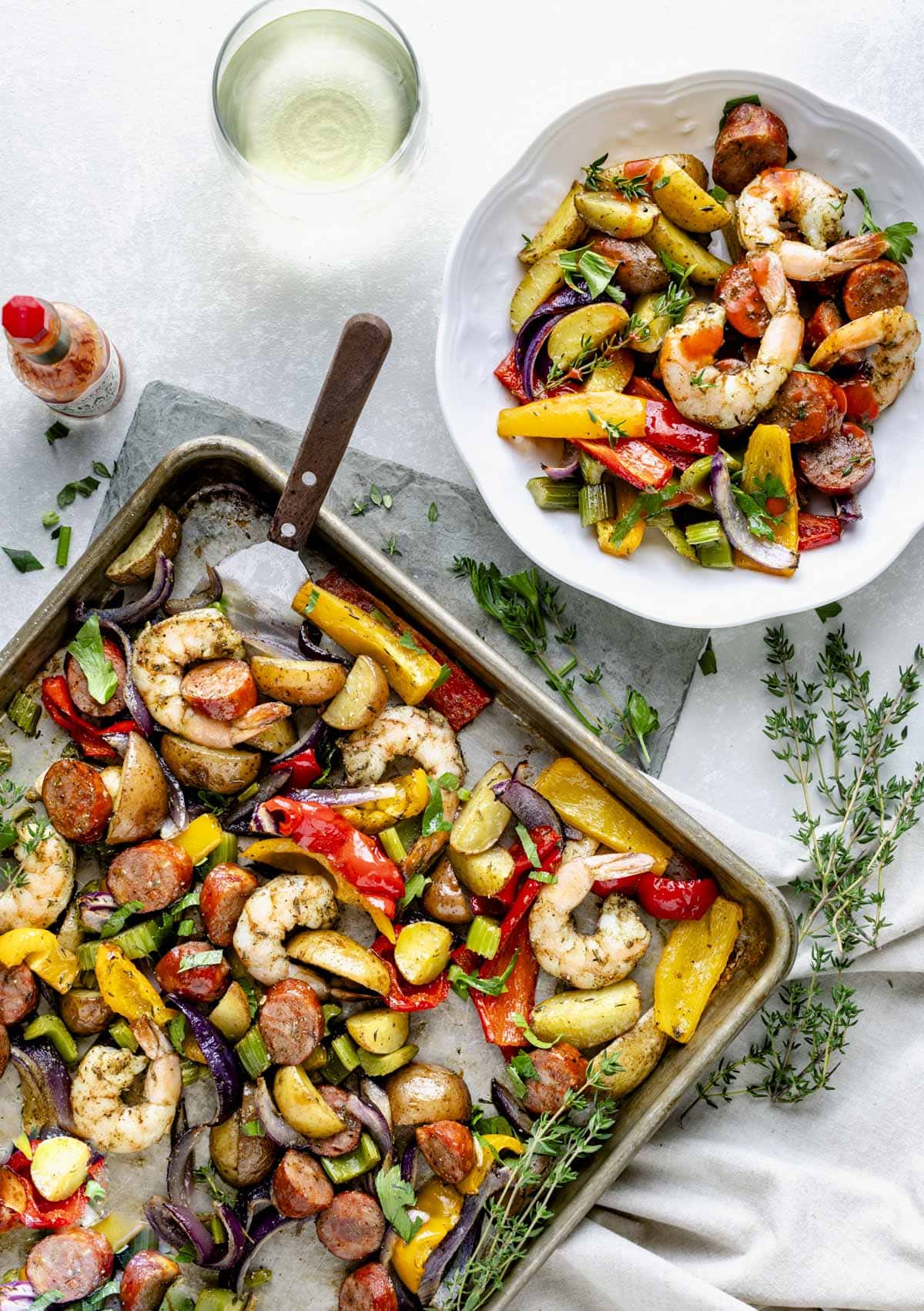 The sheet pan with the shrimp, sausage and veggies with a white bowl holding a serving off to the side