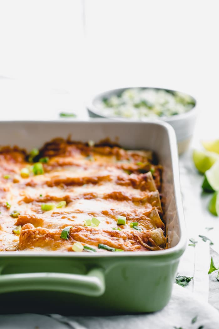 A side view of chicken enchiladas with melted cheese and scallions on top