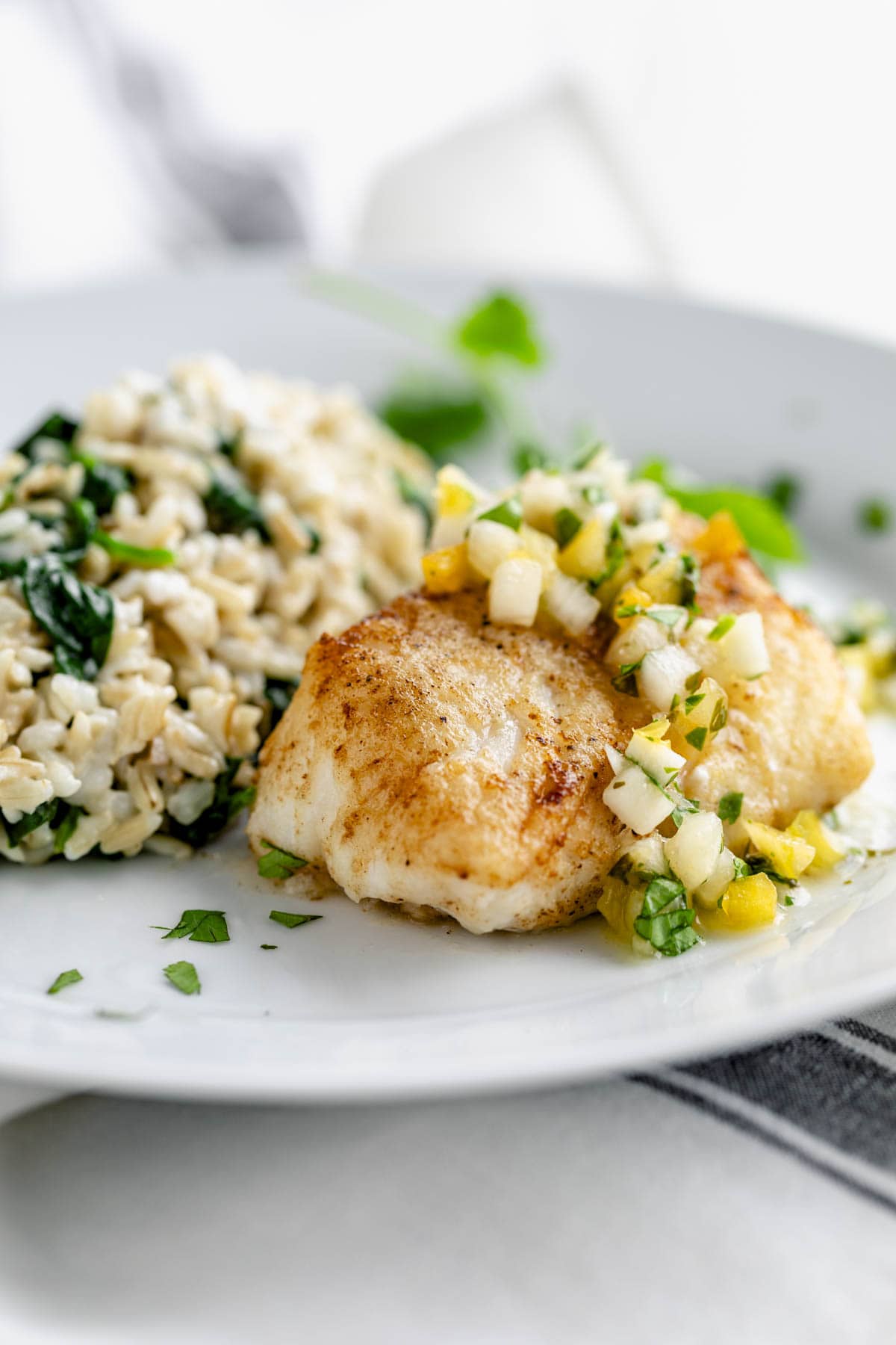 golden browned cod filet with pineapple salsa and rice on a white plate from a side angle