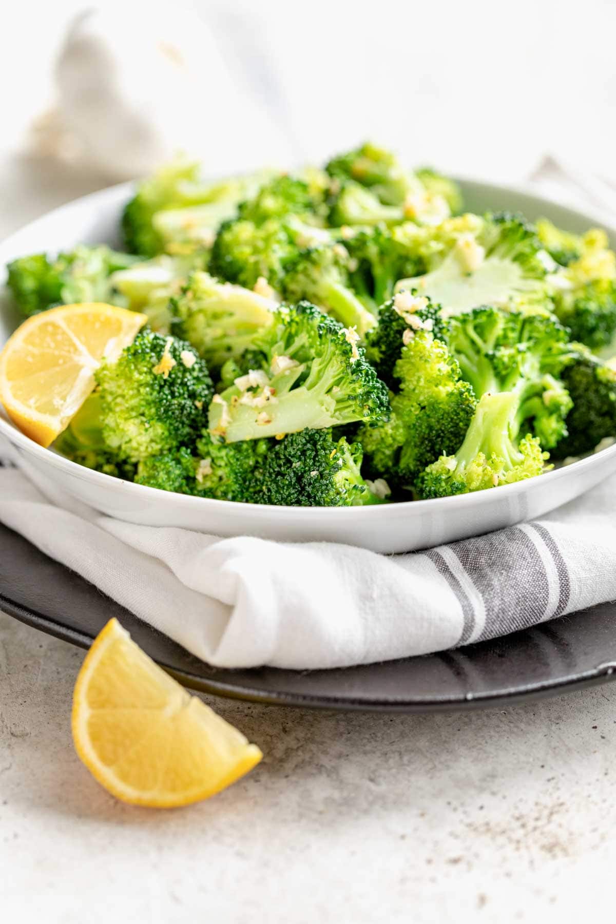 side view of bowl of broccoli with lemon wedges