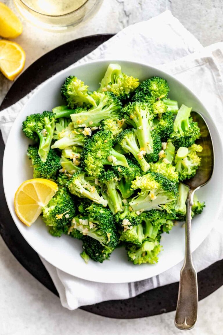 overhead white bowl with broccoli, lemon wedges and spoon
