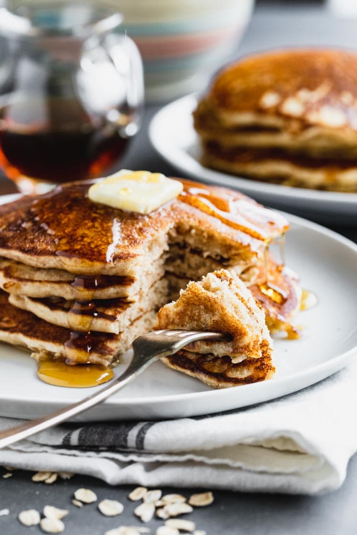 A stack of pancakes with a fork full of a bite