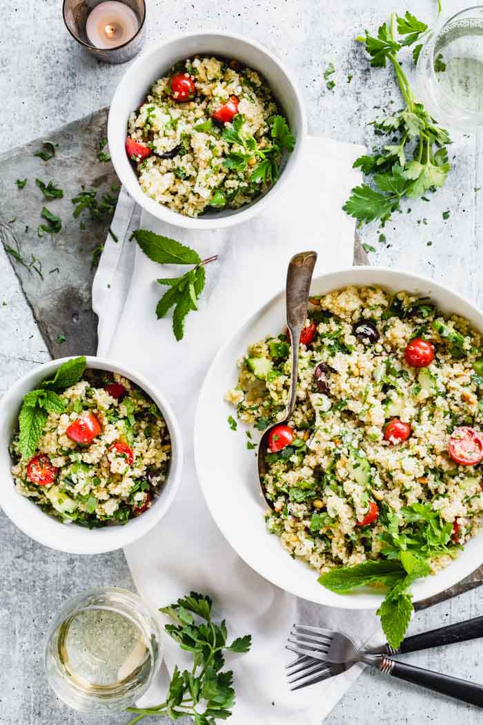 Two servings of Mediterranean quinoa salad and a serving bowl of it, from overhead