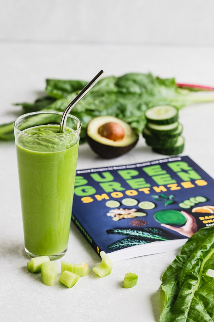 Green smoothie next to cookbook and surrounded by ingredients