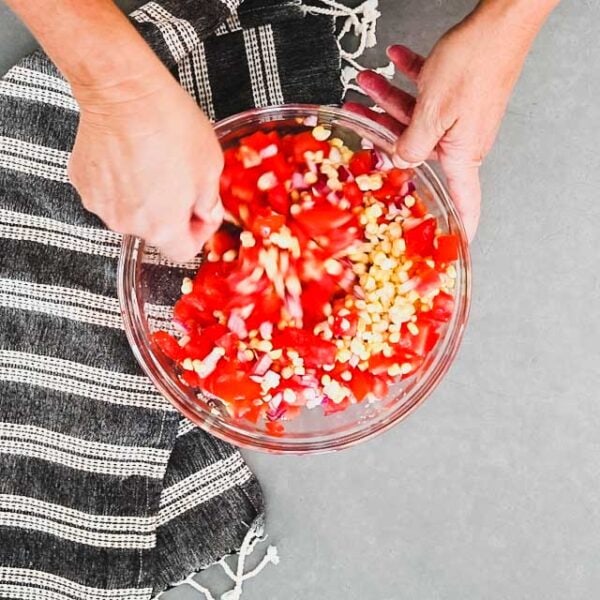 Corn, tomatoes, red onion, lime just being stirred in a small glass bowl.