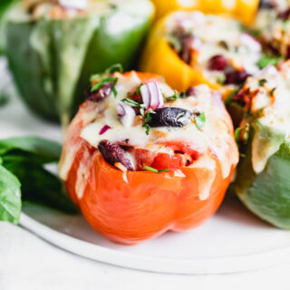 A closeup of a red bell stuffed peppers with kidney beans, red onion, basil and olives with melted cheese on top.